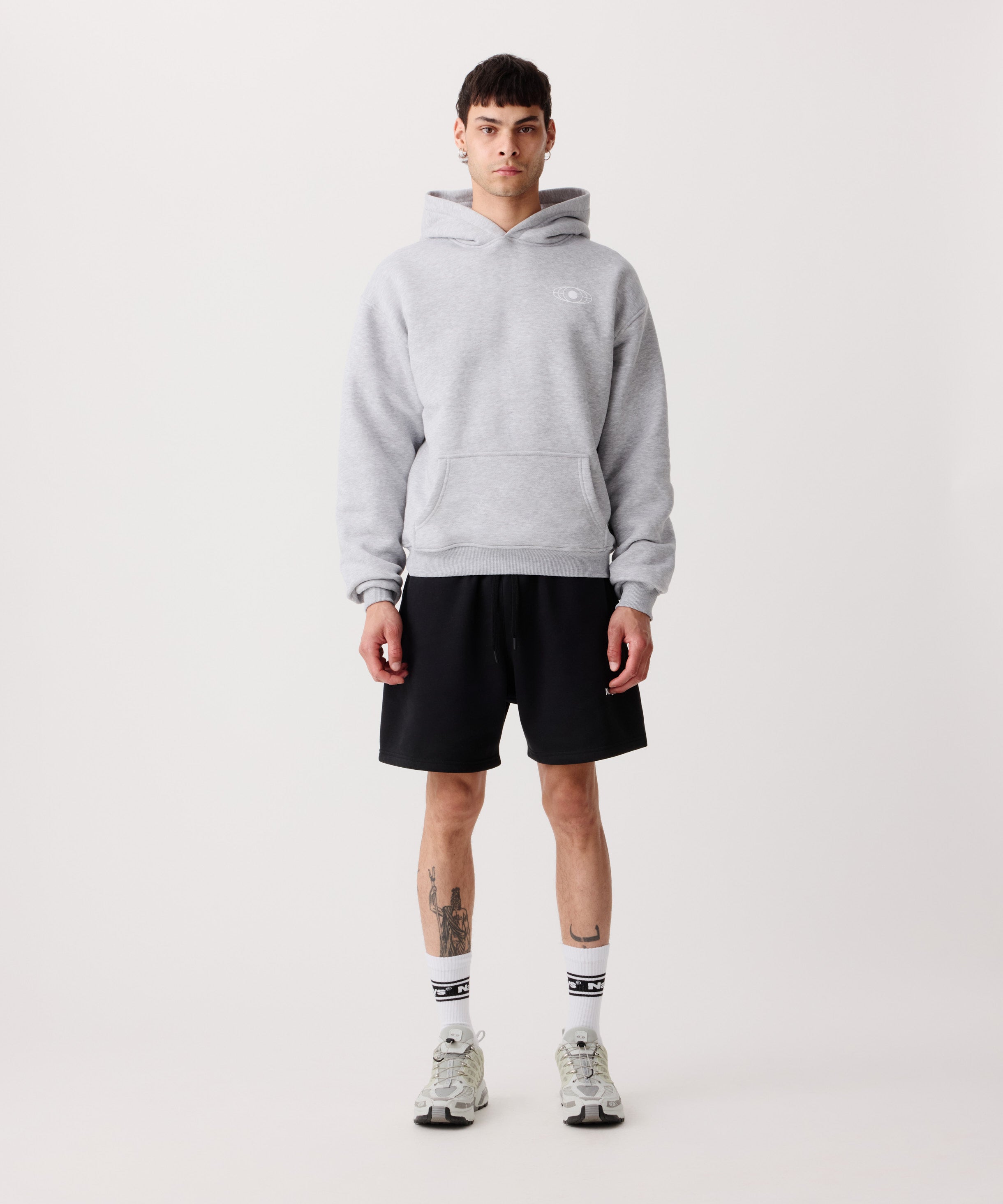 Ein hell-grauer Kapuzen-Pullover getragen von einem Mann. Er trägt dazu 
eine kurze, schwarze Hose, weiße Socken und helle Turnschuhe.