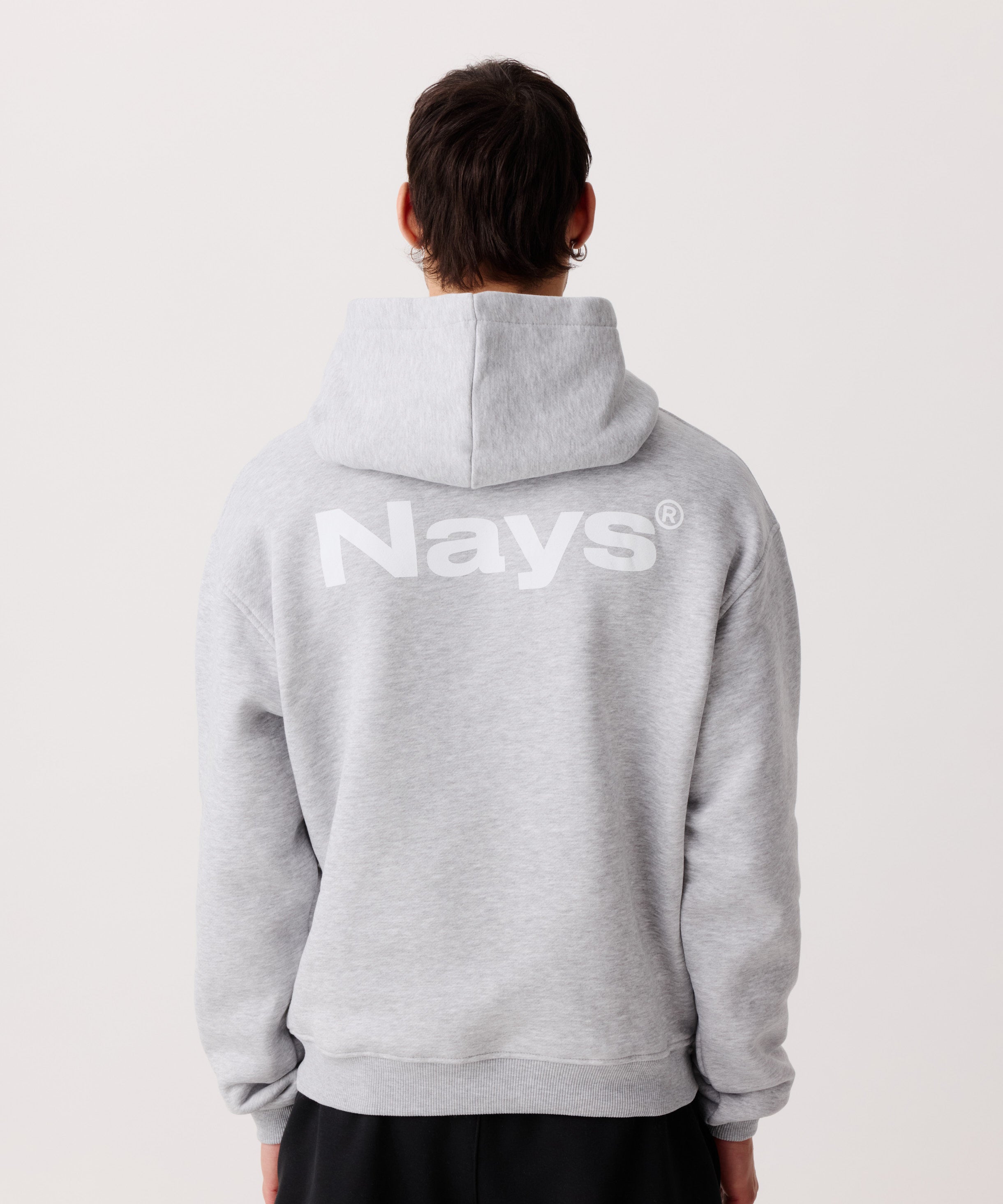 Ein hell-grauer Kapuzen-Pullover getragen von einem Mann von hinten. Deutlich zu erkennen der große Logo-Schriftzug auf dem Rücken.