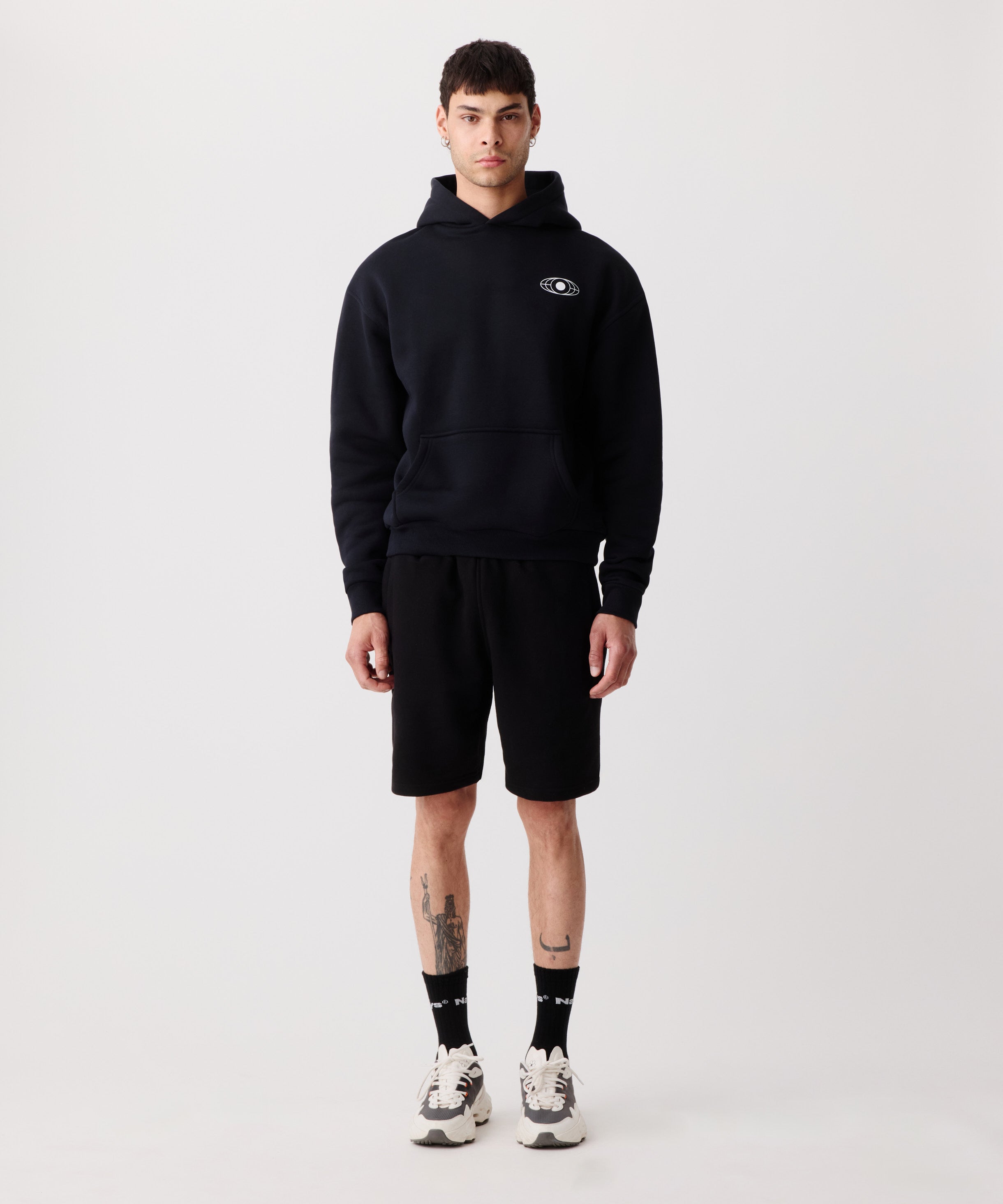 Ein schwarzer Kapuzen-Pullover getragen von einem Mann. Er trägt dazu 
eine kurze, schwarze Hose, schwarze Socken und helle Turnschuhe.
