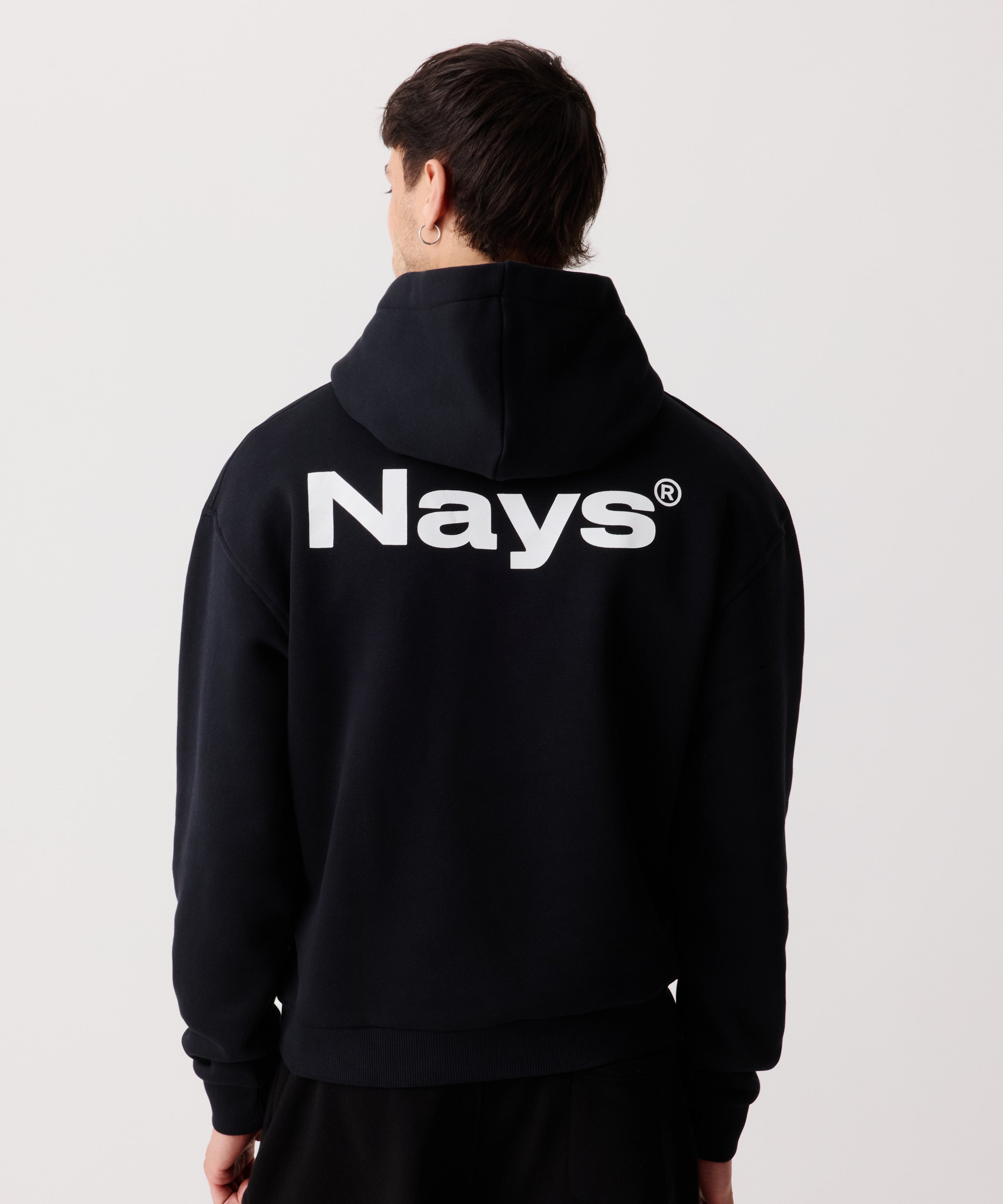Ein schwarzer Kapuzen-Pullover getragen von einem Mann von hinten. Deutlich zu erkennen der große Logo-Schriftzug auf dem Rücken in weiß.