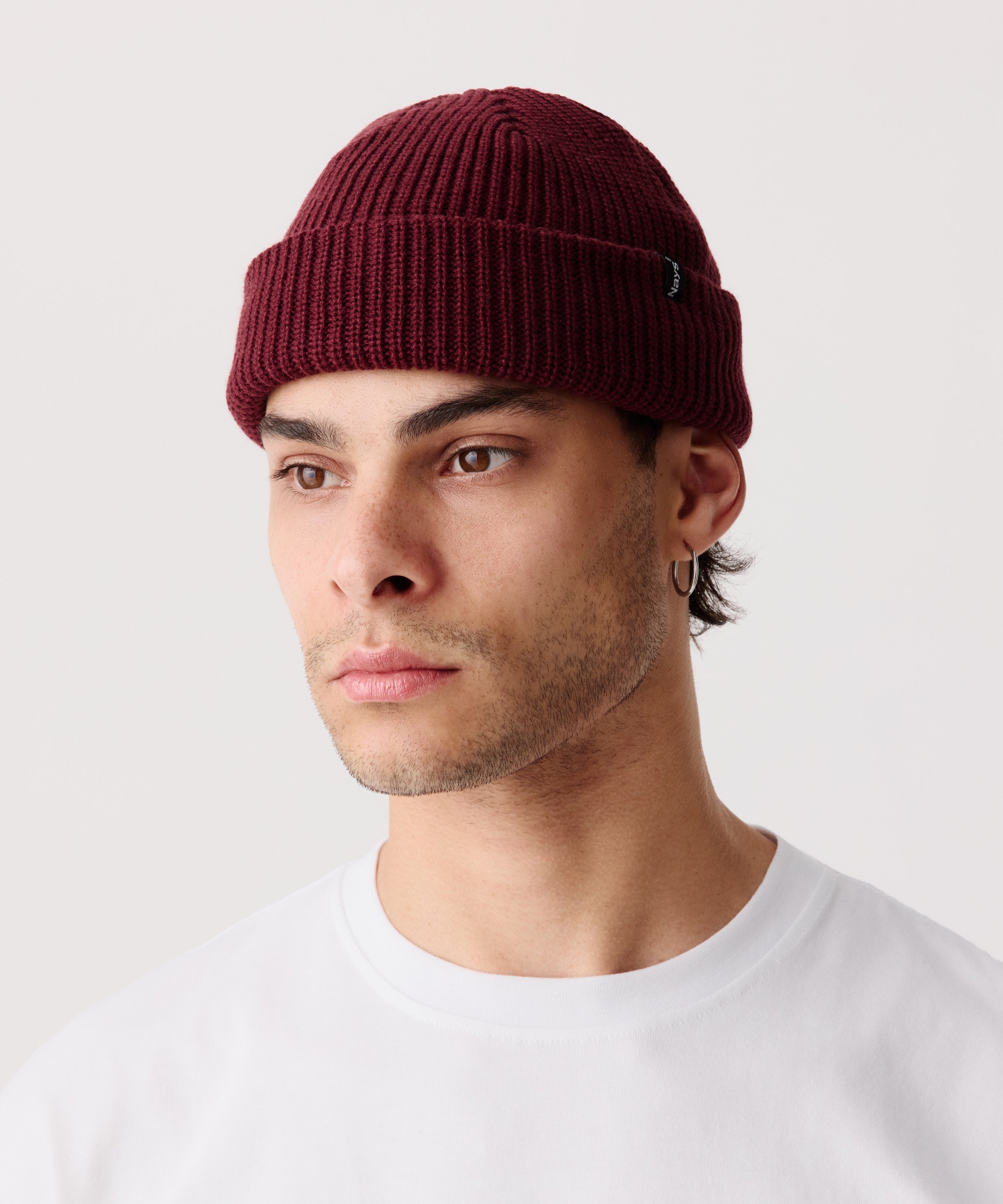 Weinrote Strickmütze mit gerippter Textur getragen von einem Mann im Halbseiten-Profil. Dazu trägt er ein weißes T-Shirt.