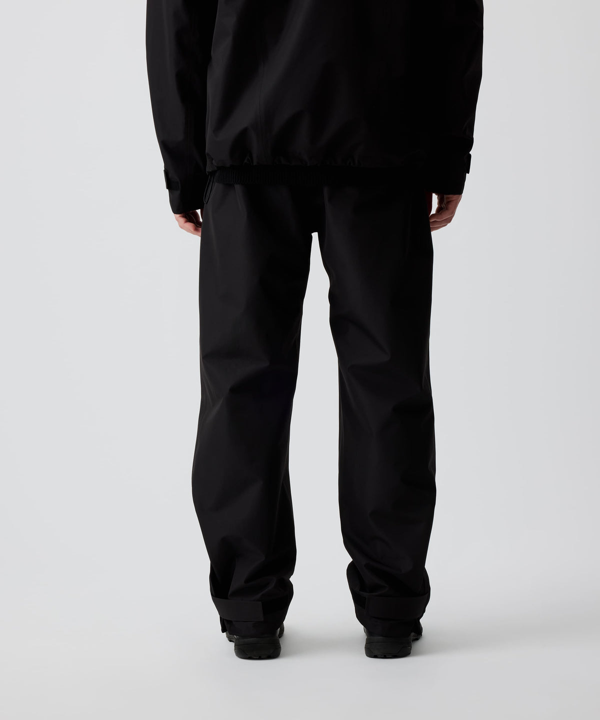 Nays 3L Multifunctional Rain Pants in der Rückansicht getragen von einer Person, zeigt ergonomische Passform und Reißverschlüsse am Beinsaum für einfaches An- und Ausziehen über Schuhe.