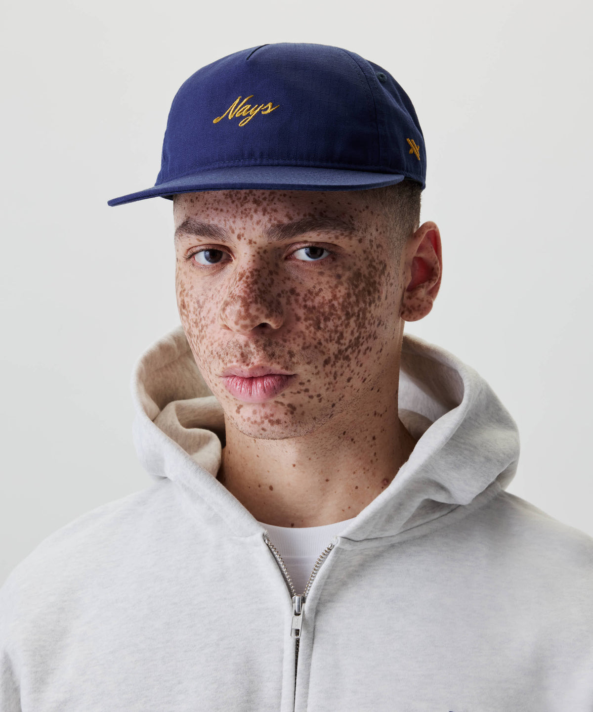 Nahaufnahme eines jungen Mannes mit Sommersprossen, der eine Ripstop Script Cap trägt. Die Kappe hat ein gesticktes gelbes Logo auf der Vorderseite.