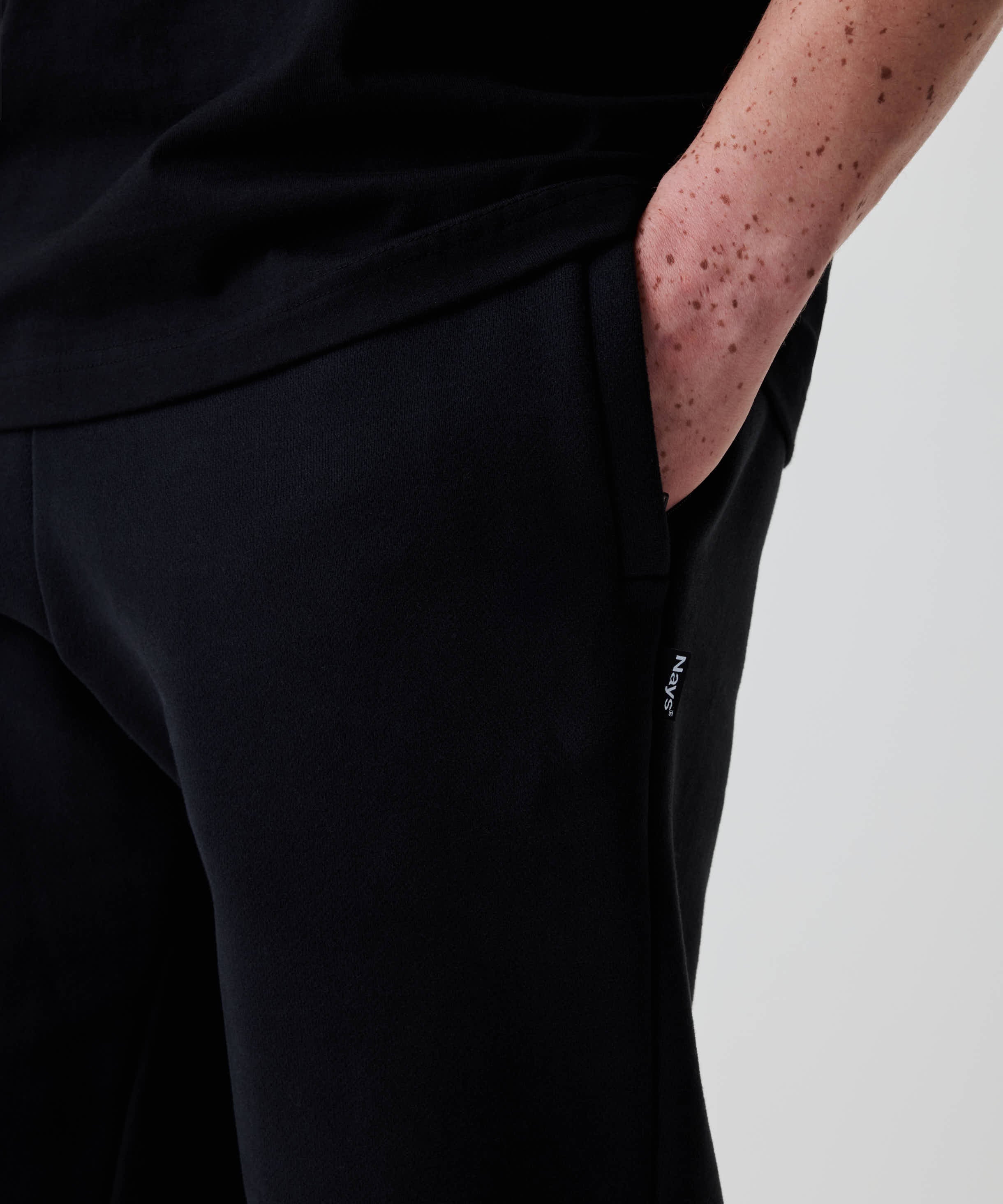 Eine freihändige Nahaufnahme zeigt Nays Classic Sweatpants in Schwarz mit Regular Fit, kleinem Label an der Seitennaht und handlicher Tasche.
