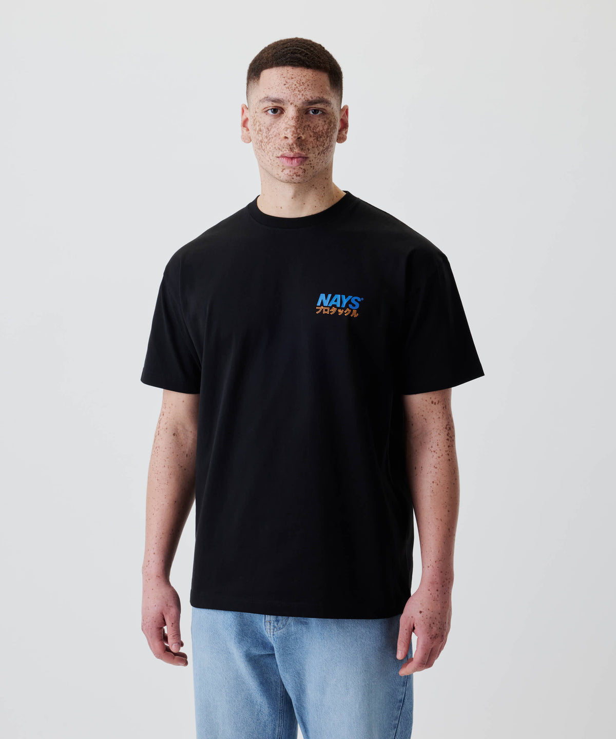 Junger Mann trägt das Nays Pro Tackle International Tee mit kleinem Logo und japanischen Schriftzeichen auf der Brust, kombiniert mit hellblauen Jeans.