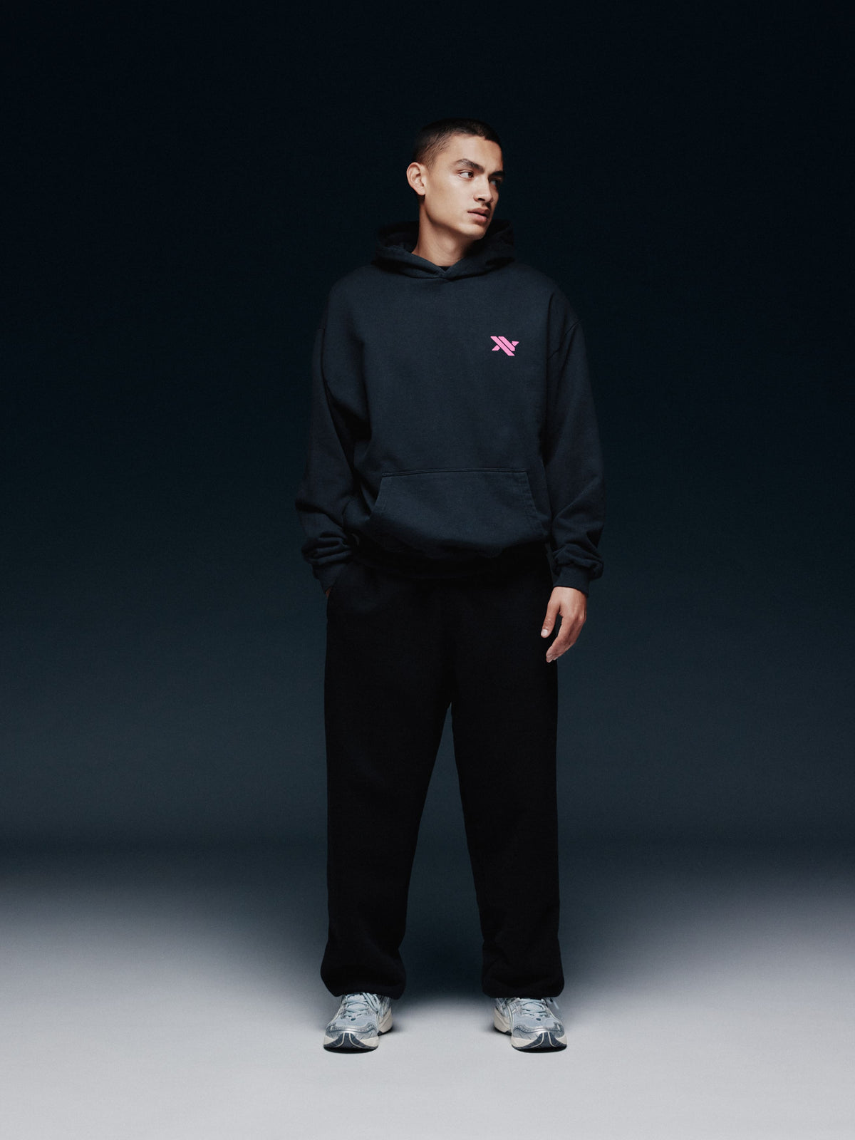 Model trägt den schwarzen NAYS TRN Hoodie in Frontansicht mit rosa Logo.