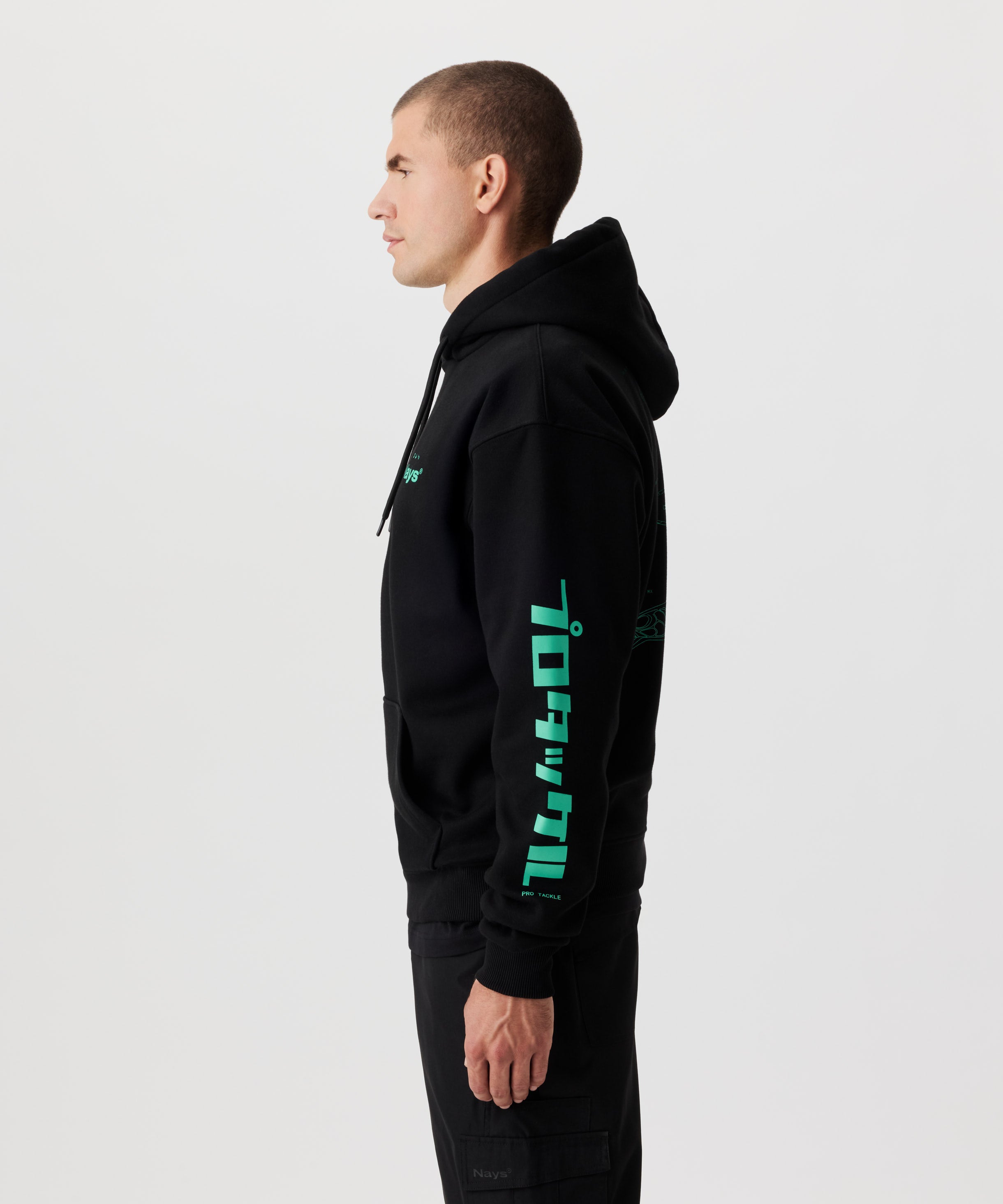 Seitenansicht Mann im schwarzen Kapuzen-Sweatshirt mit grünen Prints auf der Brust und beiden Ärmeln.