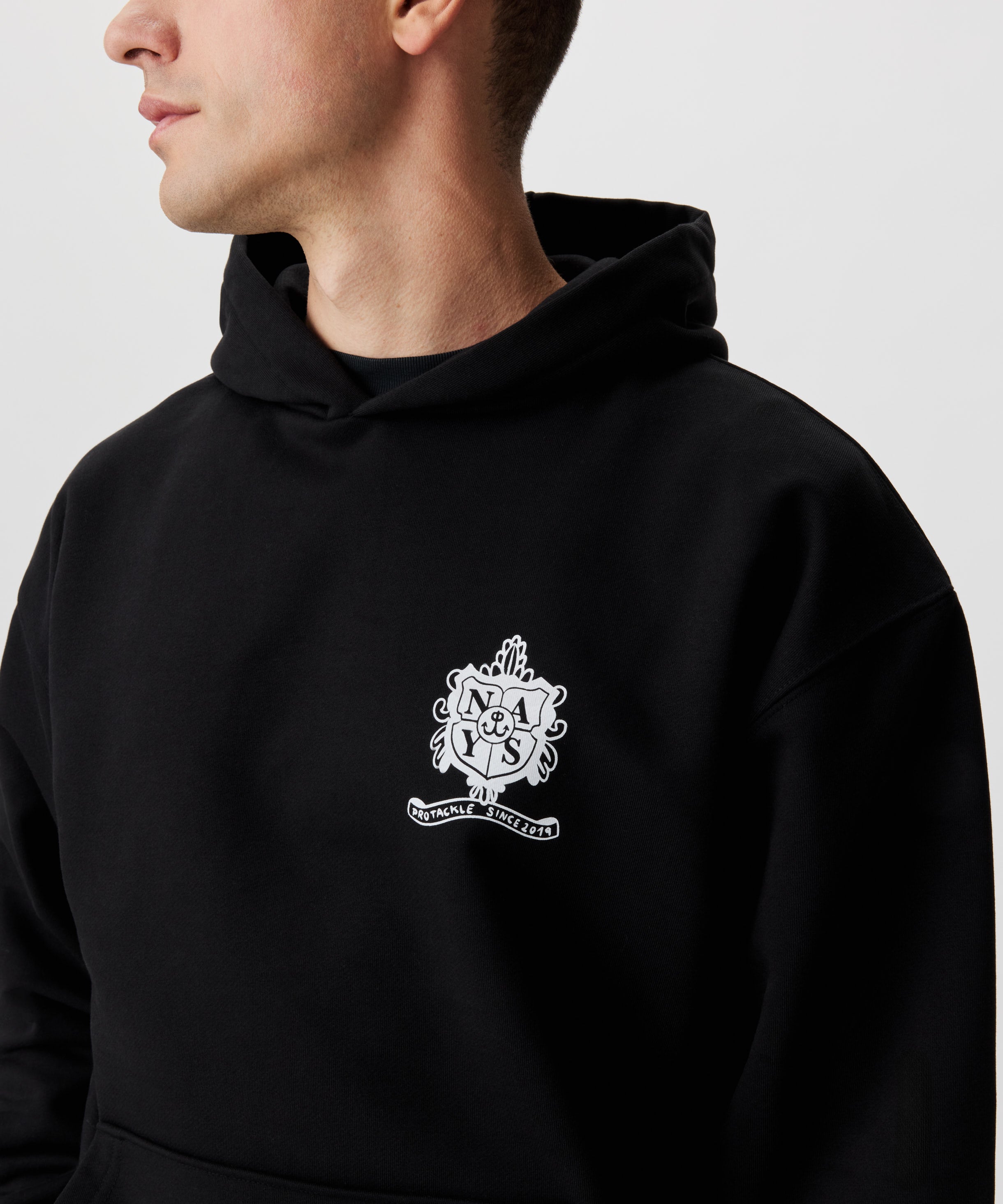 Frontansicht Mann im schwarzen Kapuzen Sweatshirt. Das Sweatshirt hat einen Druck auf der linken Brust in weiß.