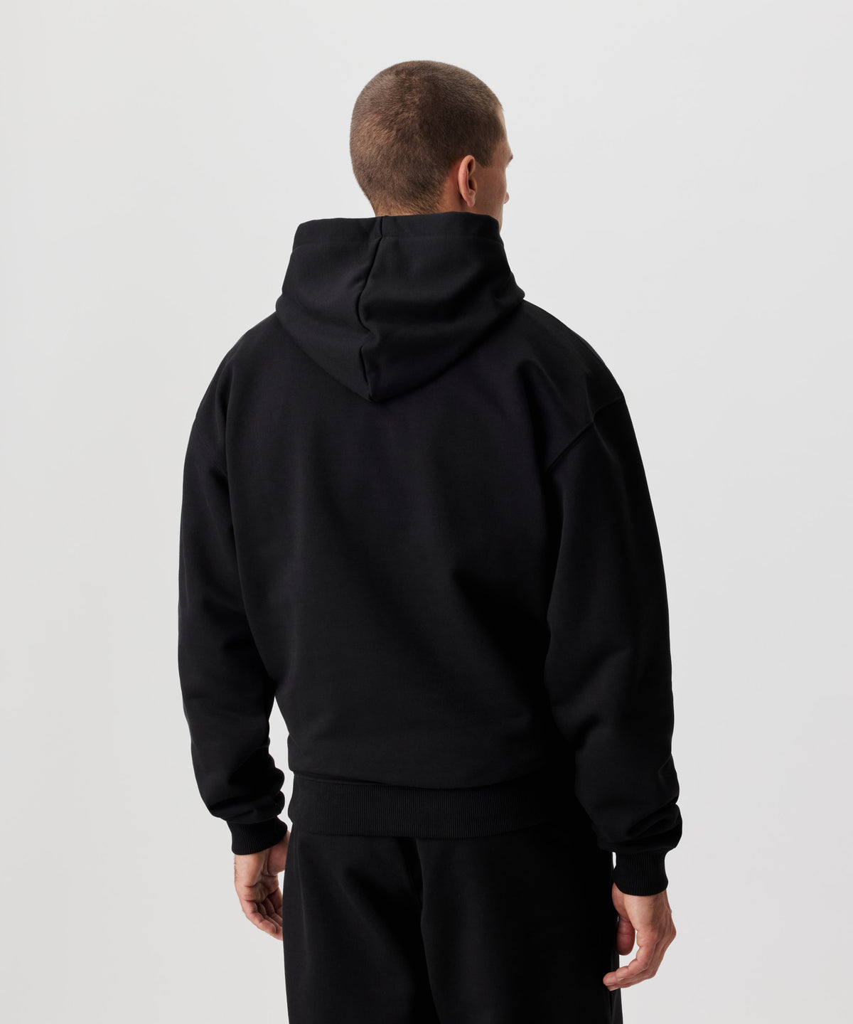 Rückansicht Mann im schwarzen Kapuzen Sweatshirt und schwarzer Hose. 