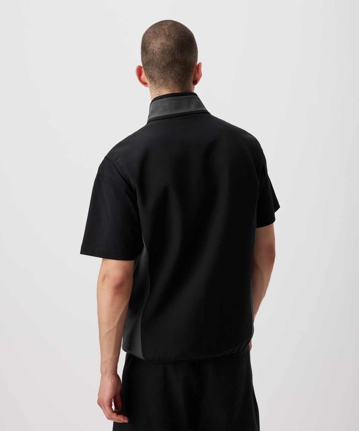 Ein Mann von hinten zu sehen trägt eine dünne, funktionelle Weste in schwarz. Die Seiten und der Kragen sind farblich in grau abgesetzt.