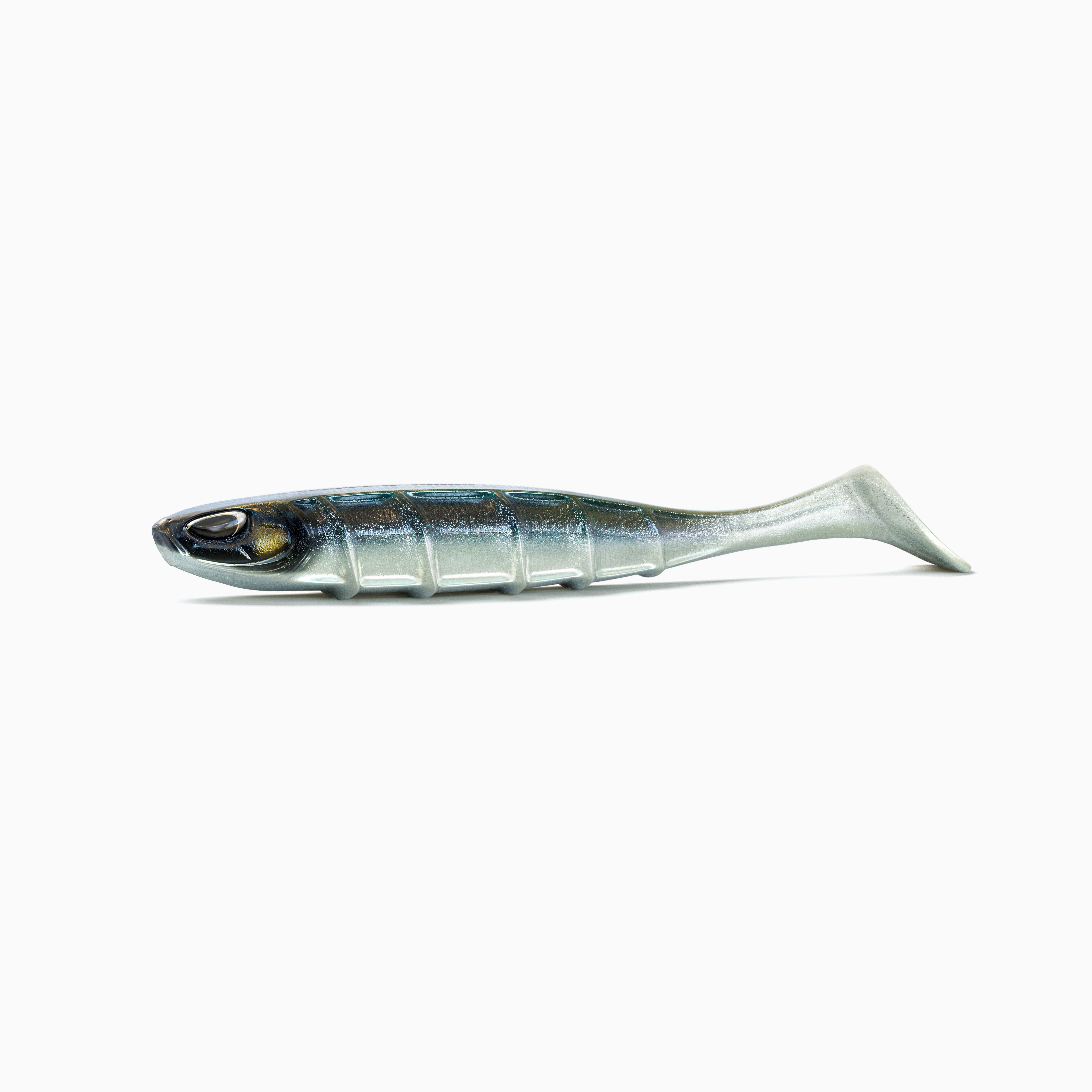 Ein Angelköder in Form eines Fisches liegt waagerecht auf weißem Hintergrund. Der silberne Körper hat einen dunklen, blau-grün schimmernden Rücken und zeigt seitlich feine Schuppenmuster mit einer sichtbaren Rippenstruktur. Die Augen sind realistisch gestaltet, mit schwarzen Pupillen und goldenen Akzenten. Am hinteren Ende befindet sich ein voluminöser Schaufelschwanz.