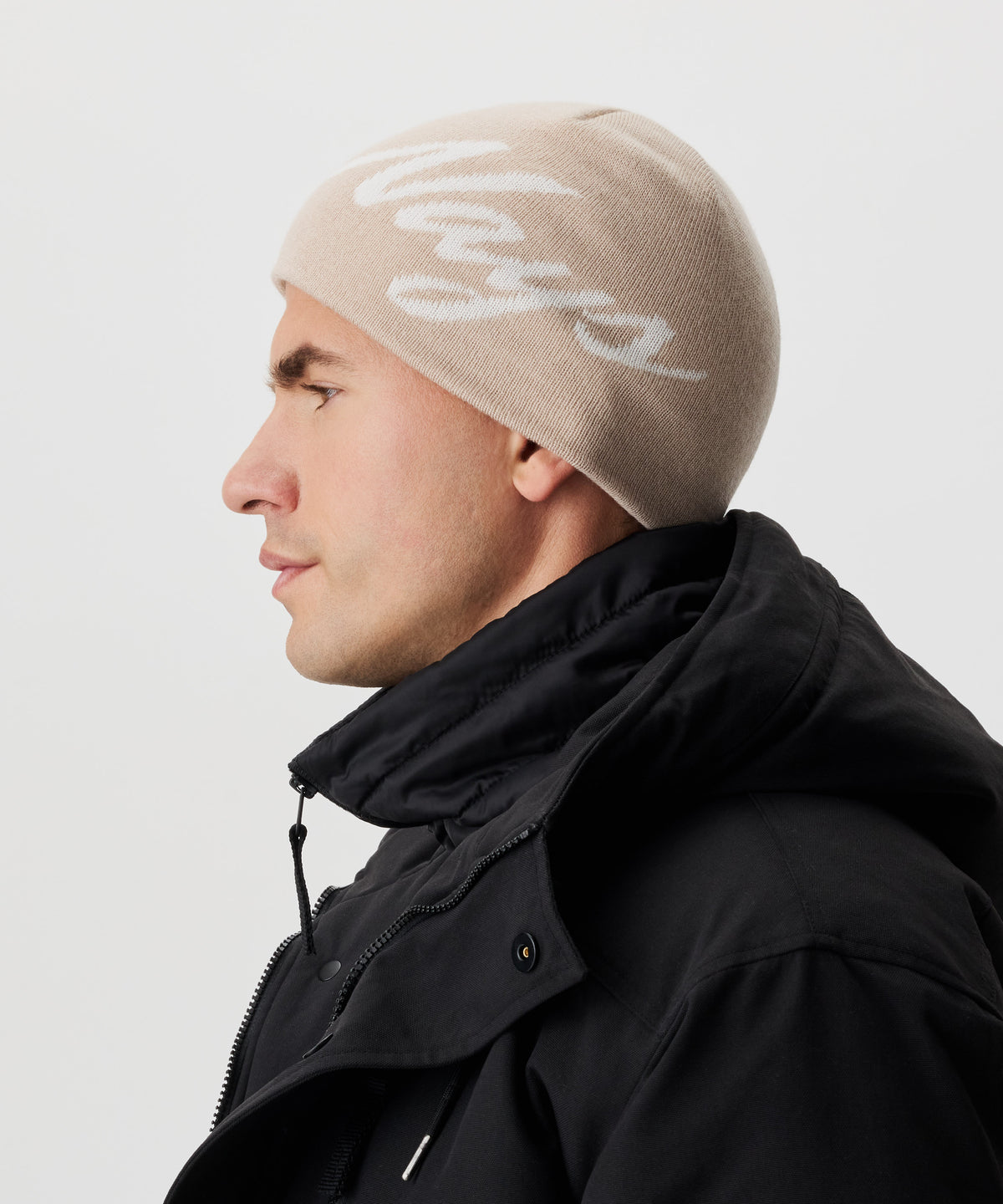 Seitliche Ansicht Mann in schwarzer Jacke und beige-farbiger Strickmütze mit weißem Nays-Logo-Schriftzug.