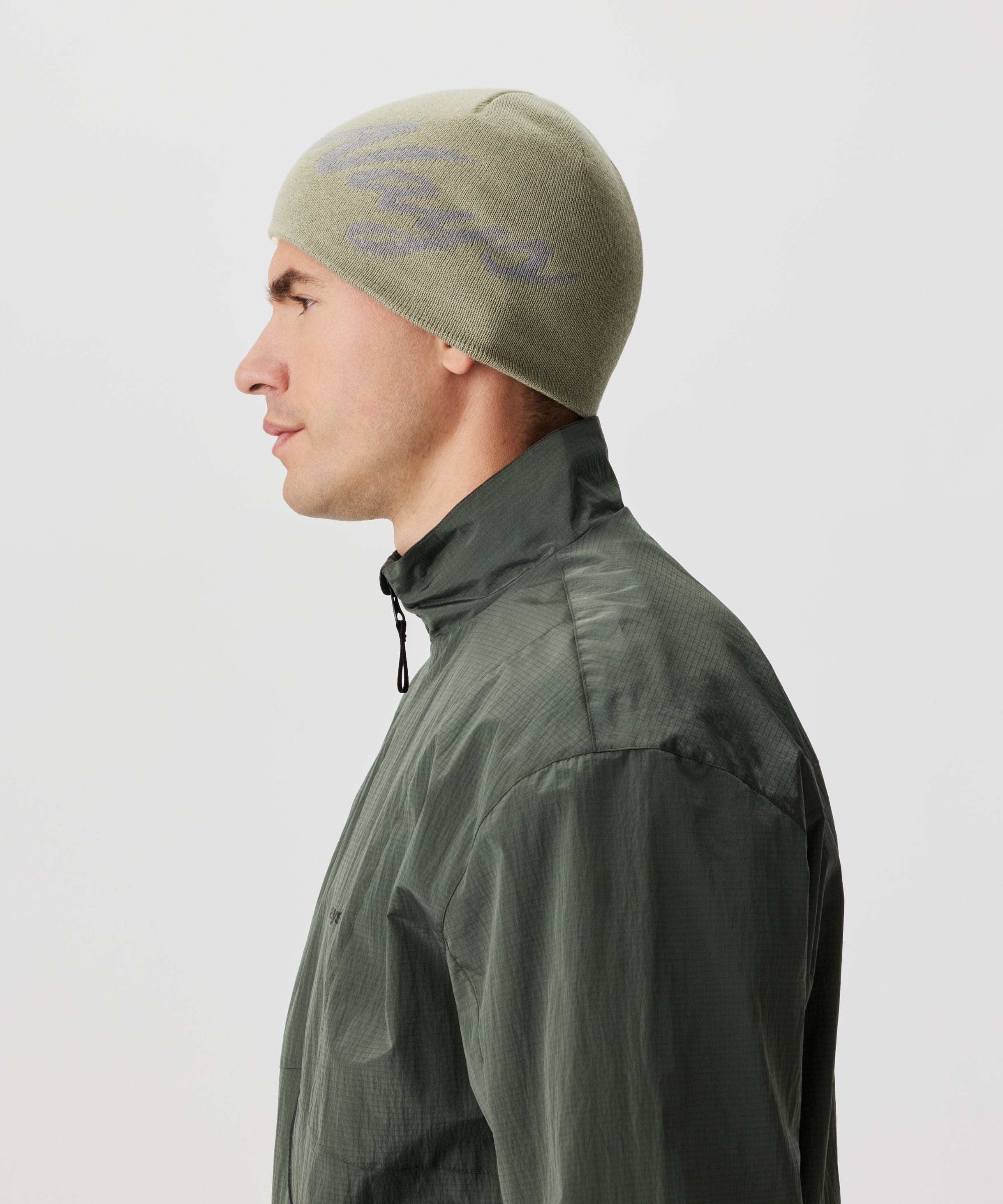 Seitliche Ansicht Mann in grüner Jacke und grüner Strickmütze mit grauem Nays-Logo-Schriftzug.
