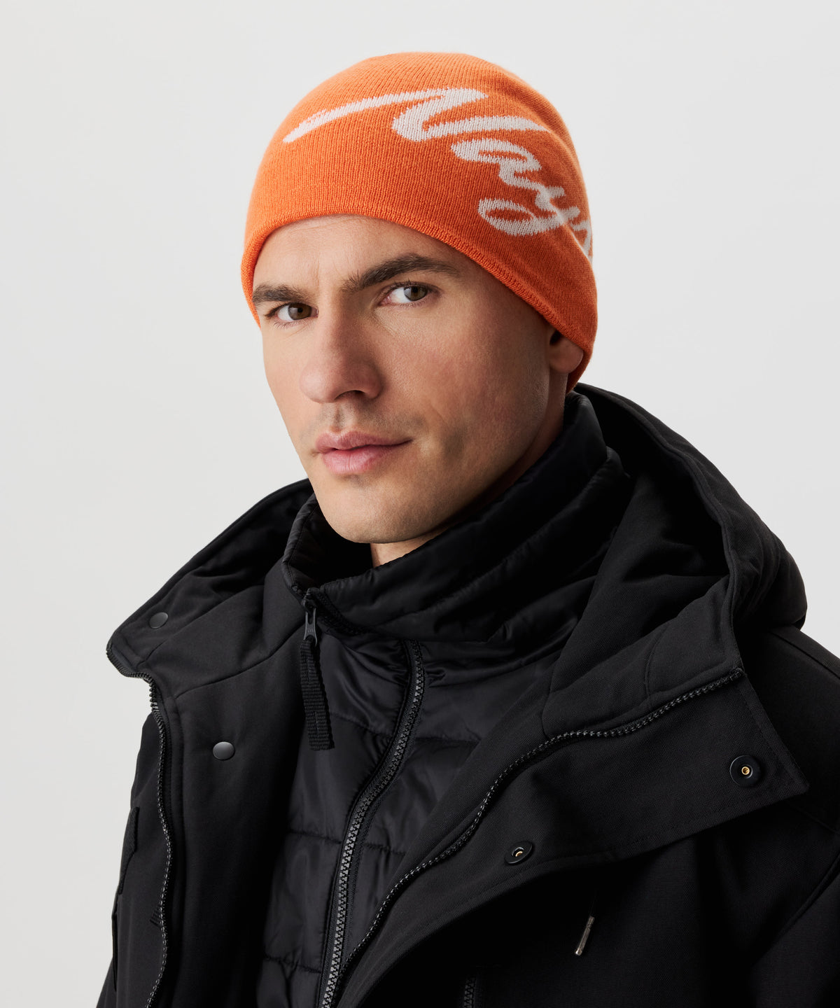 Frontansicht Mann  in schwarzer Jacke und orange-farbiger Strickmütze mit weißem Nays-Logo-Schriftzug.