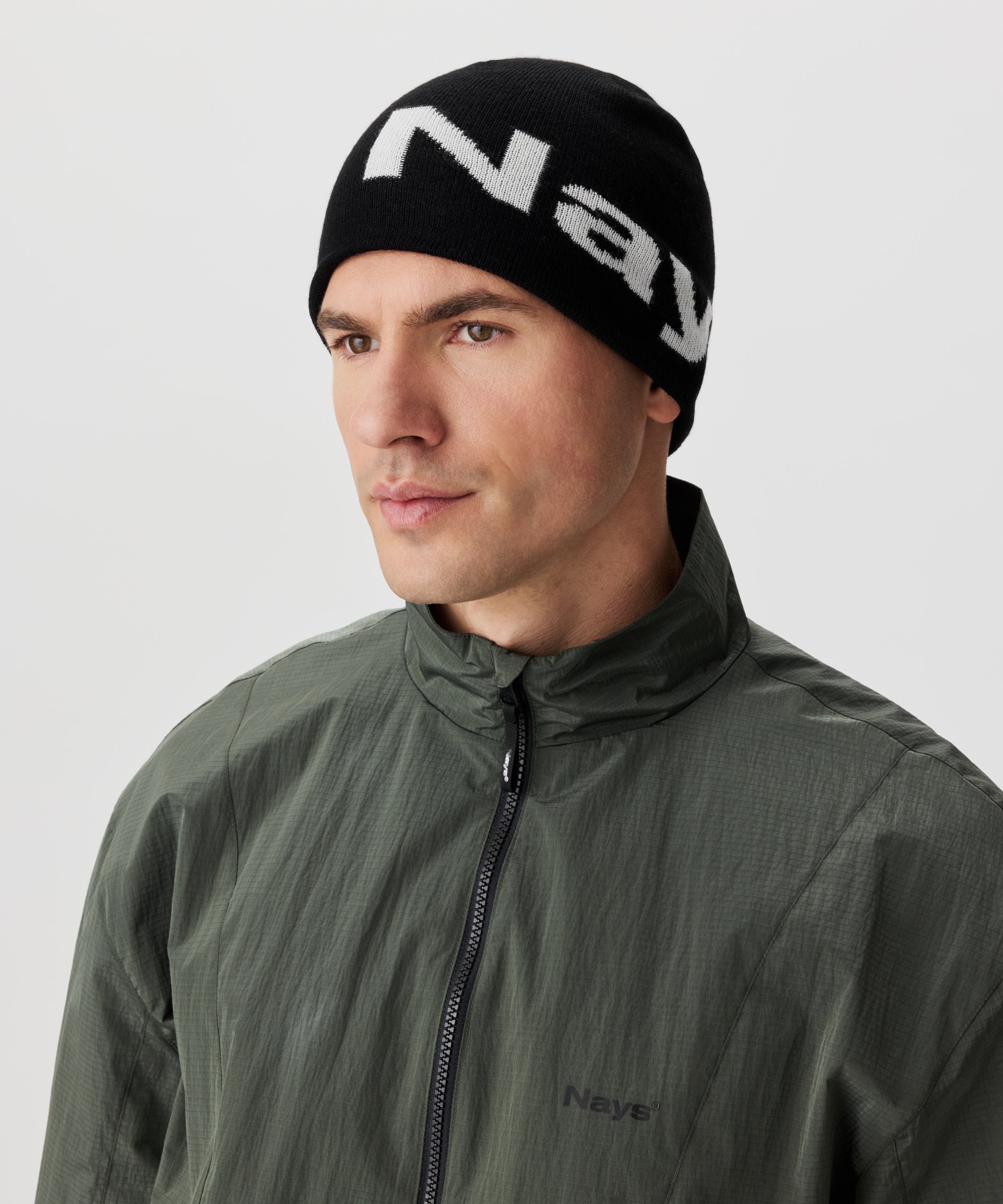 Frontansicht Mann in grüner Jacke und schwarzer Strickmütze mit weißem Nays-Logo-Schriftzug.
