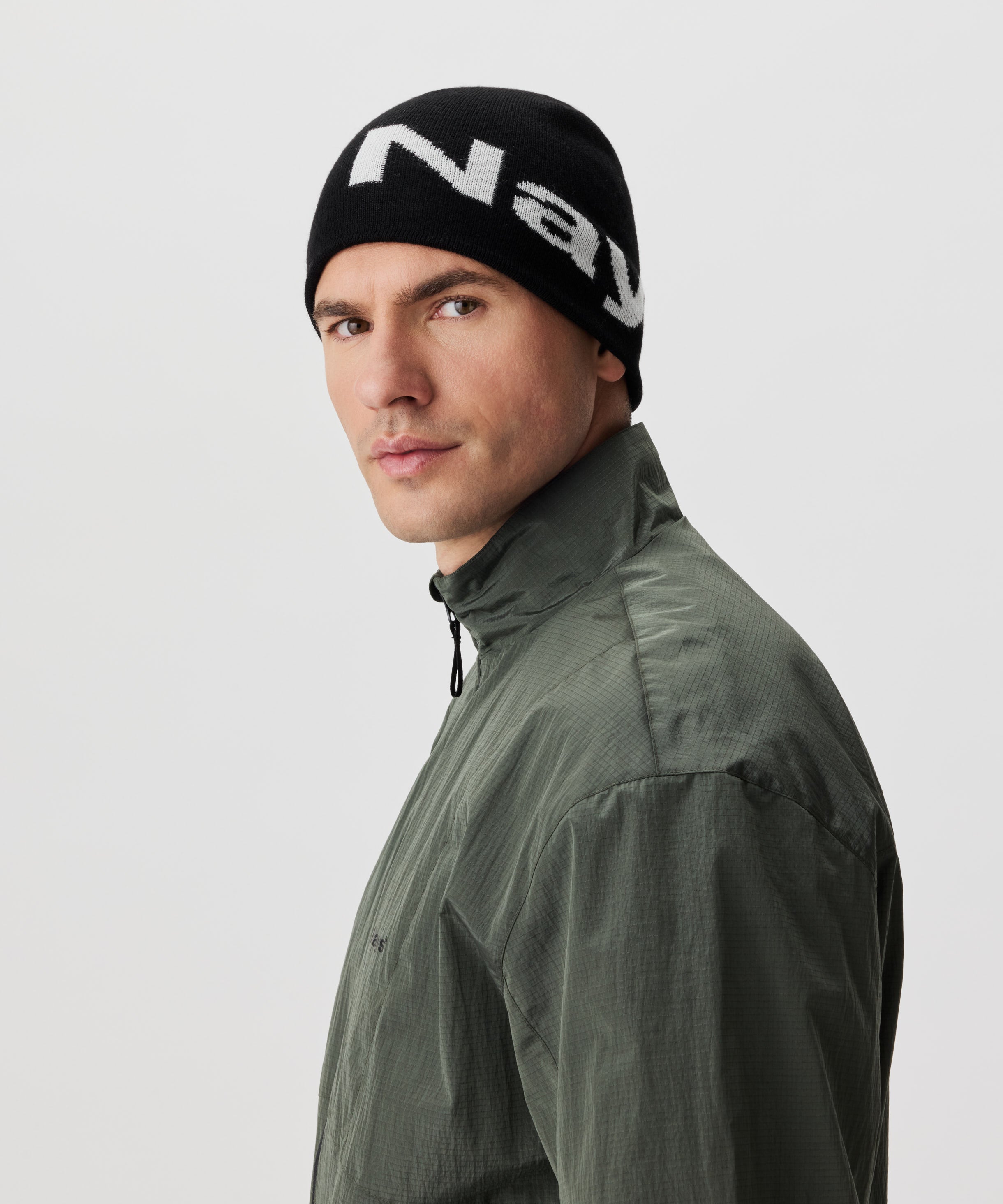 Halbseitliche Ansicht Mann in grüner Jacke und schwarzer Strickmütze mit weißem Nays-Logo-Schriftzug.
