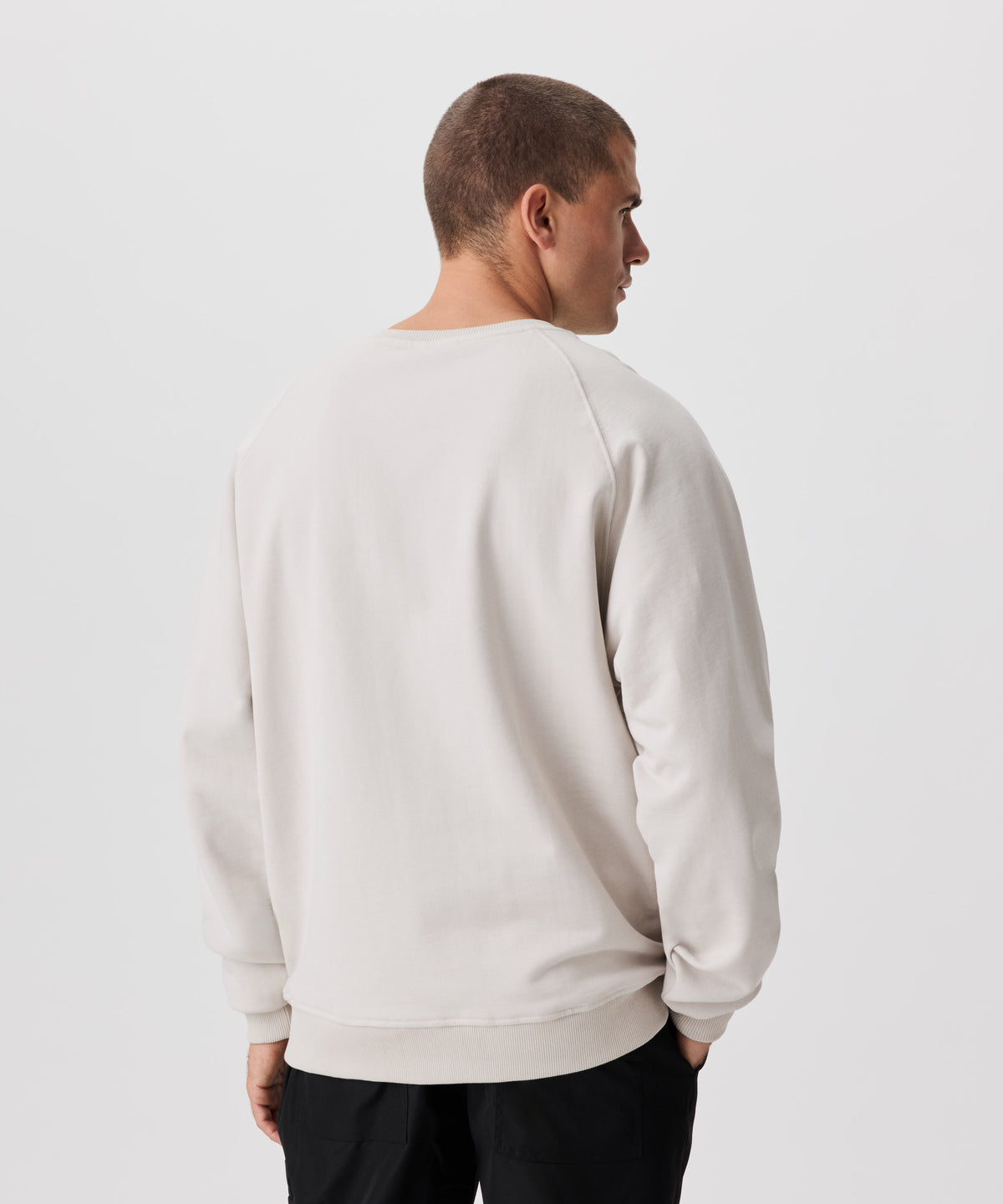 Rückansicht Mann mit mit beigefarbenem Pullover und schwarzer Hose.