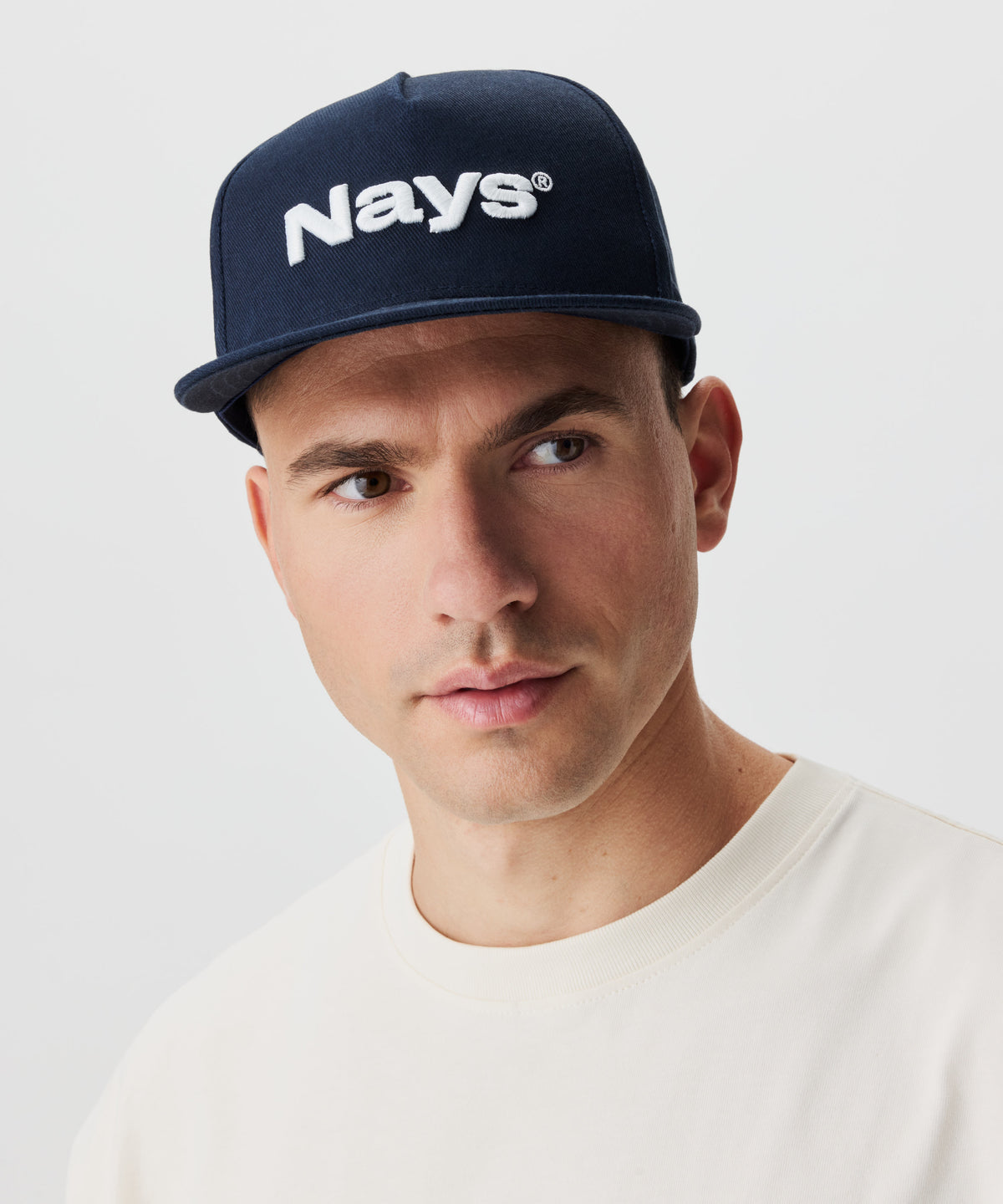 Frontansicht Mann mit Cap. Die Cap ist blau mit einem weißen Nays-Logo Strick.