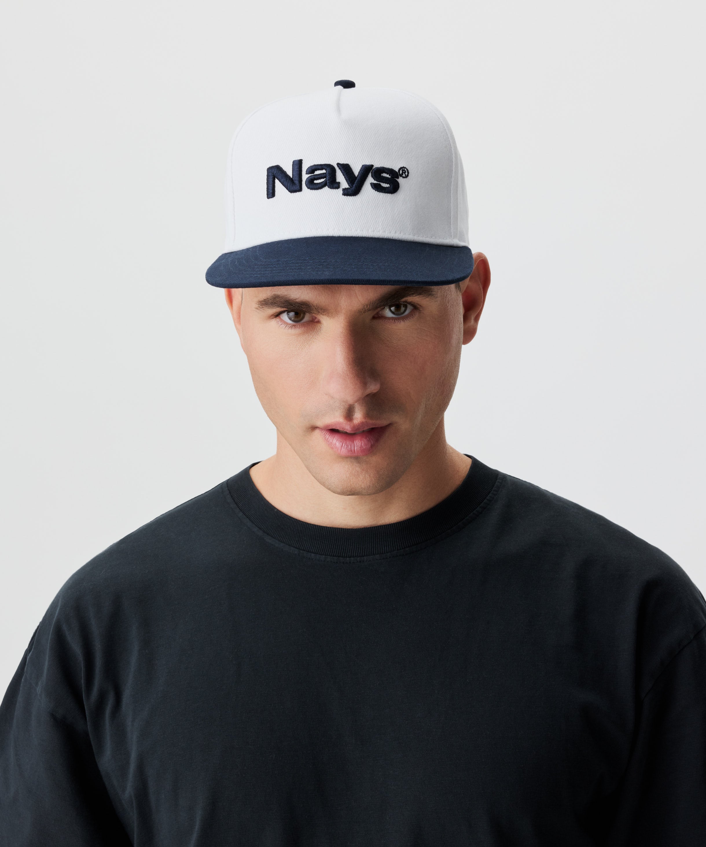 Frontansicht Mann mit Cap. Die Cap ist weiß mit blauem Schirm und einem blauen Nays-Logo Strick.