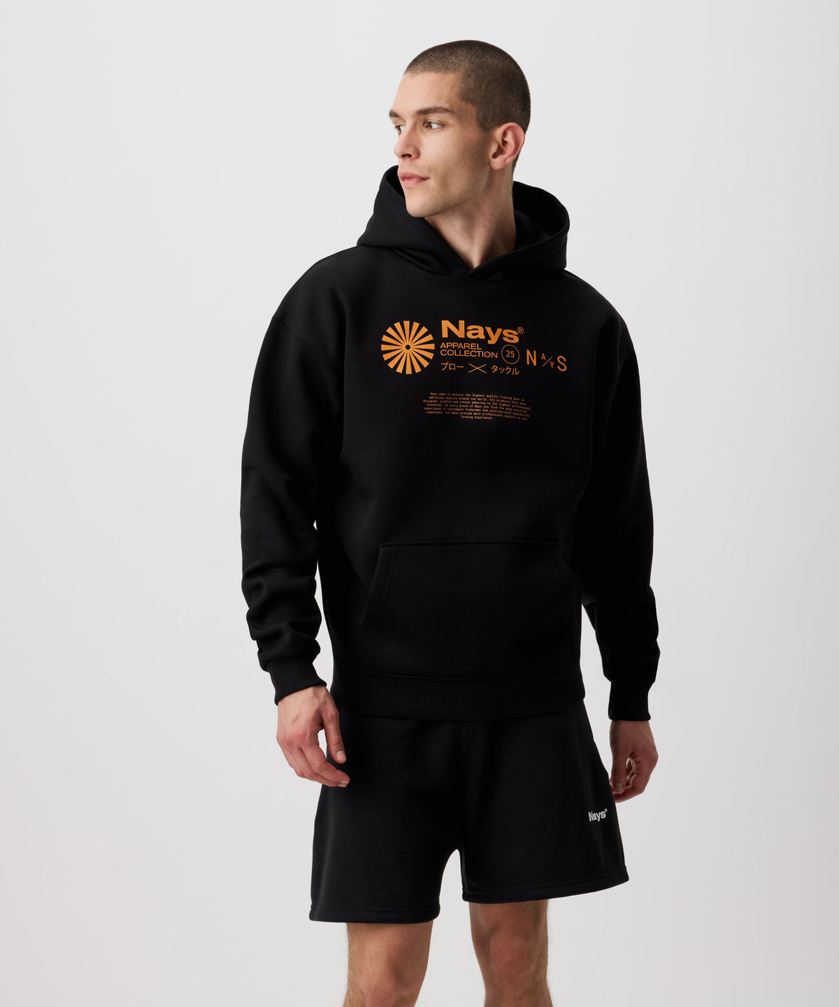 Ein schwarzer Kapuzen-Pullover mit kontrastreichen Prints in einem leuchtenden Orange, getragen von einem Mann. Der Print besteht aus einem runden, sonnenartigen Symbol und daneben tonale Nays Logo Schriftzüge.