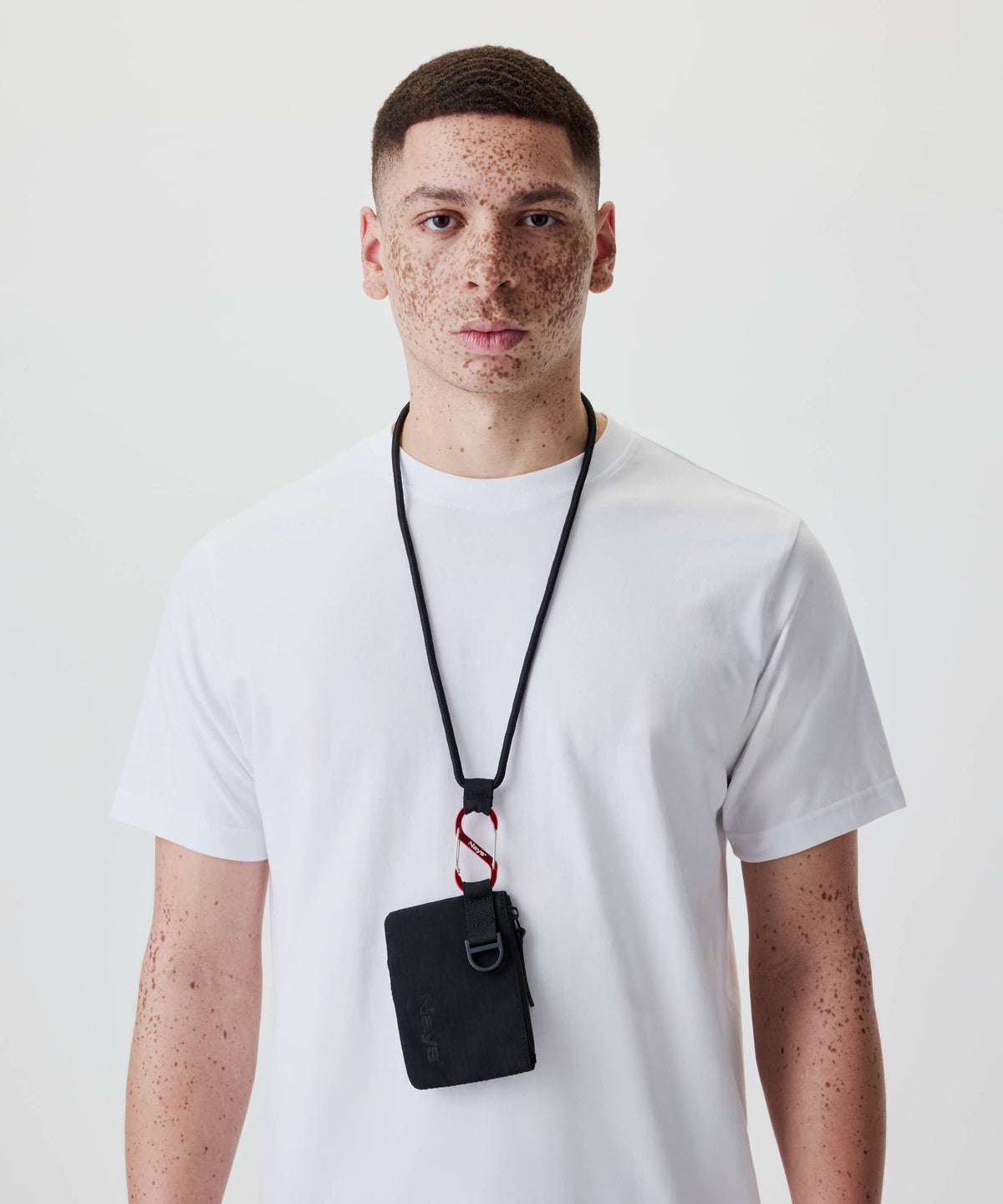 Ein junger Mann trägt das Nays Neck Pouch aus Ripstop, mit Reißverschlussfach und Mesh-Tasche, an einem schwarzen Band um den Hals.