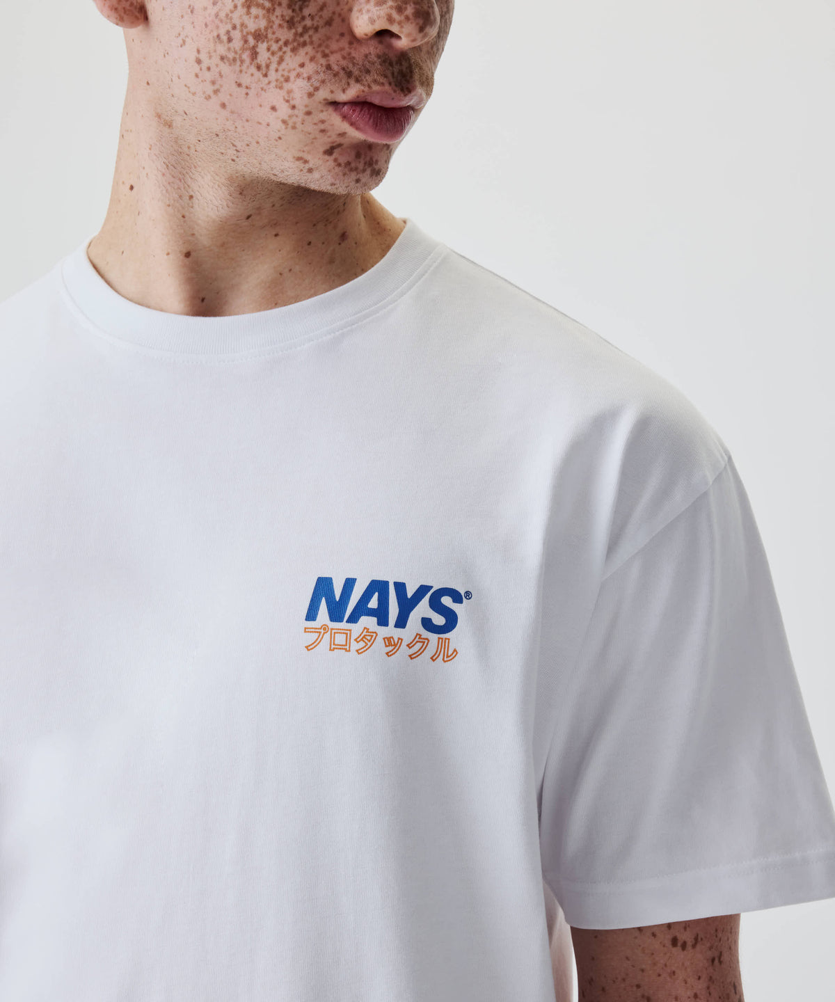 Person trägt das Nays Pro Tackle International Tee, mit freiem Logo und japanischem Schriftzug auf der Brust. Hergestellt aus 100% Baumwolle für Komfort.